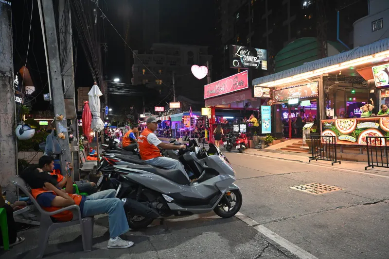 Conducteurs de moto-taxi en gilet orange attendant près de scooters garés dans une rue thaïlandaise de nuit