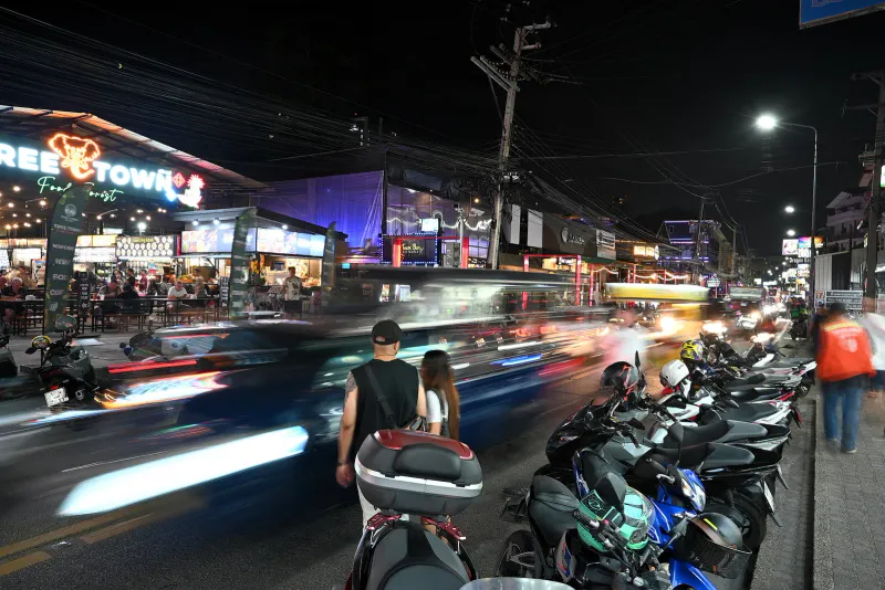 Rangée de scooters et de casques garés au bord d'une rue animée de nuit dans une station balnéaire thaïlandaise