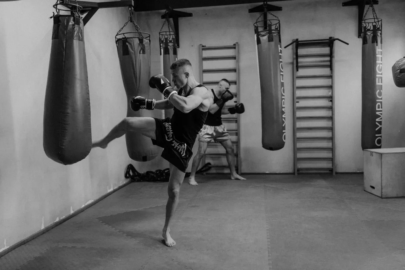 Two men training with punching bags in a dimly lit gym, the bag rounds included in a Jun Muay Thai drop-in session