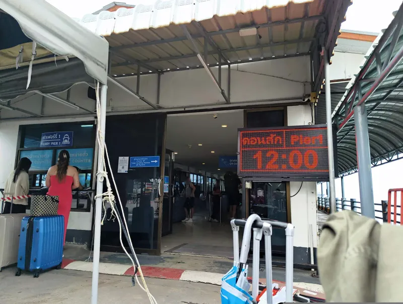 Guichets de billets et panneau des départs à l'embarcadère de Nathon, à Koh Samui, avec voyageurs et valises
