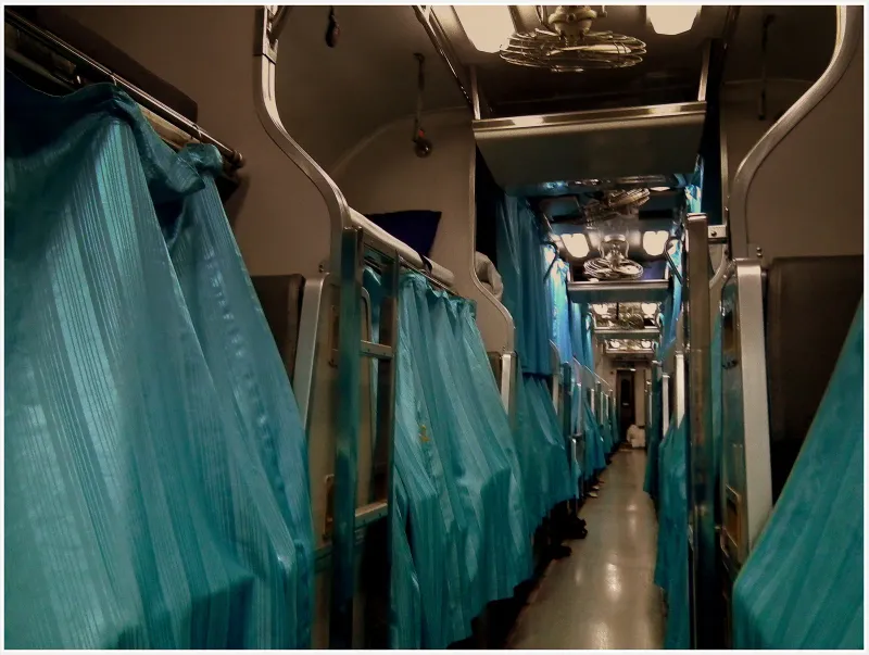 Couloir d'un wagon-lits thaïlandais de nuit, rideaux vert sarcelle tirés devant les couchettes