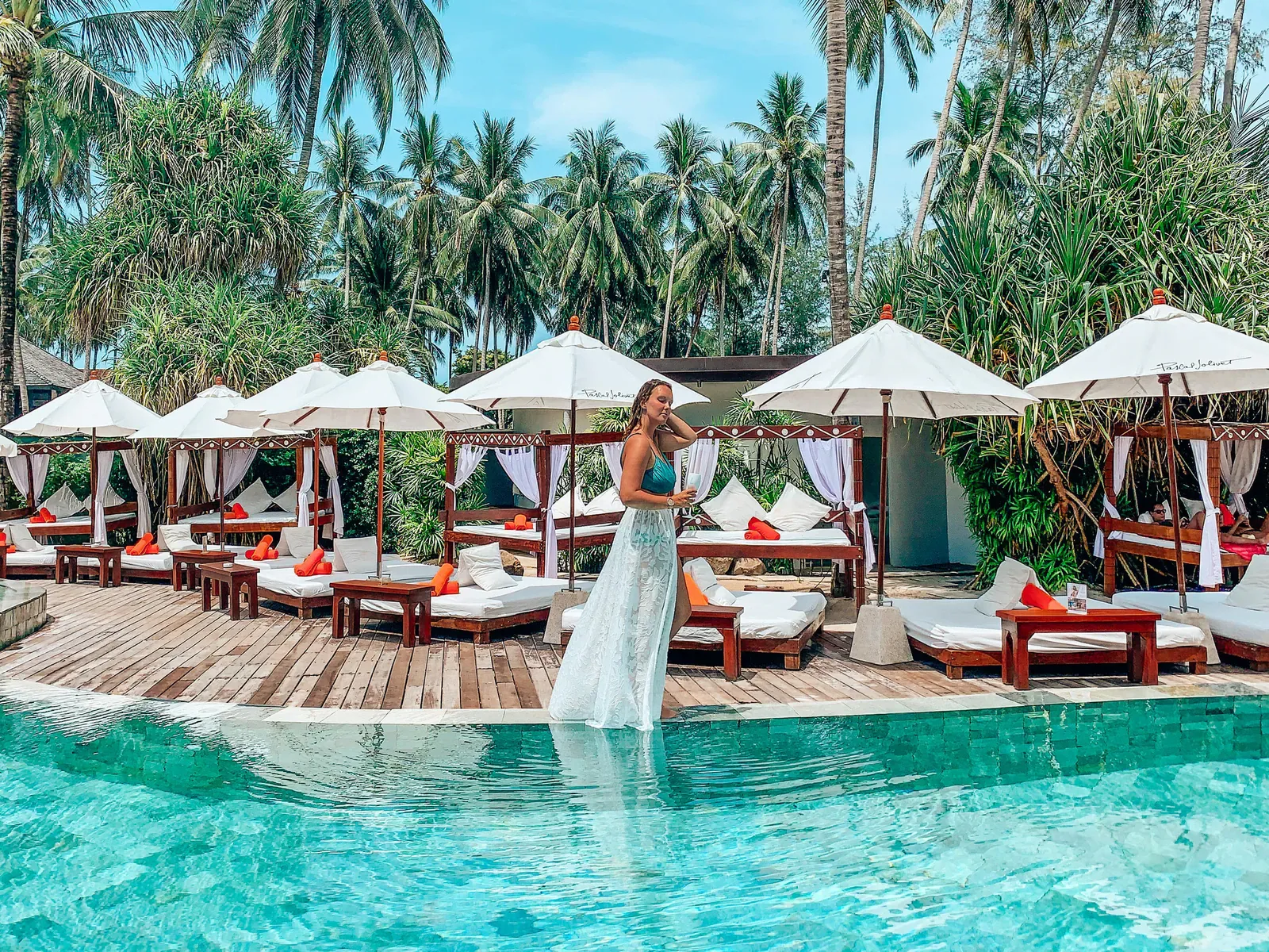A guest walking beside the infinity pool at Nikki Beach Koh Samui, lined with white daybeds and umbrellas