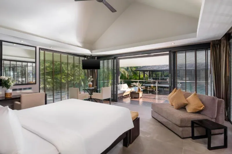 A suite at Nikki Beach Koh Samui with a bed, lounge area and view toward the pool
