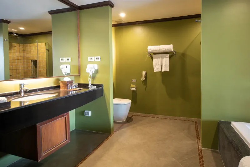 Salle de bains d'une chambre deluxe du Nora Buri Resort avec baignoire, plan de toilette sombre et murs verts