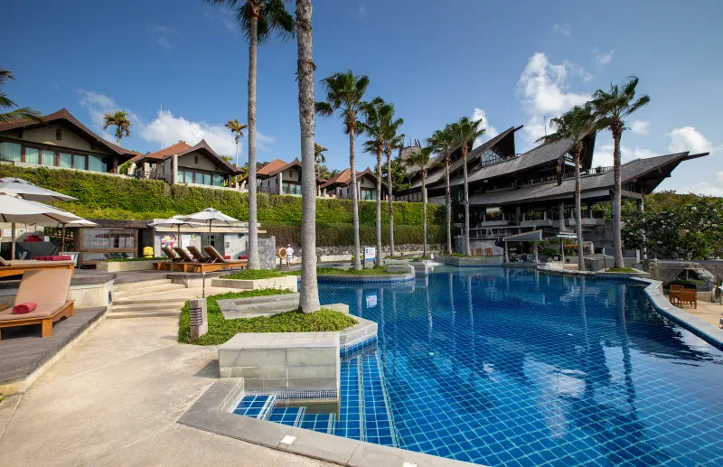 Piscine à débordement bleue incurvée avec transats sous les toits de bois du Nora Buri Resort