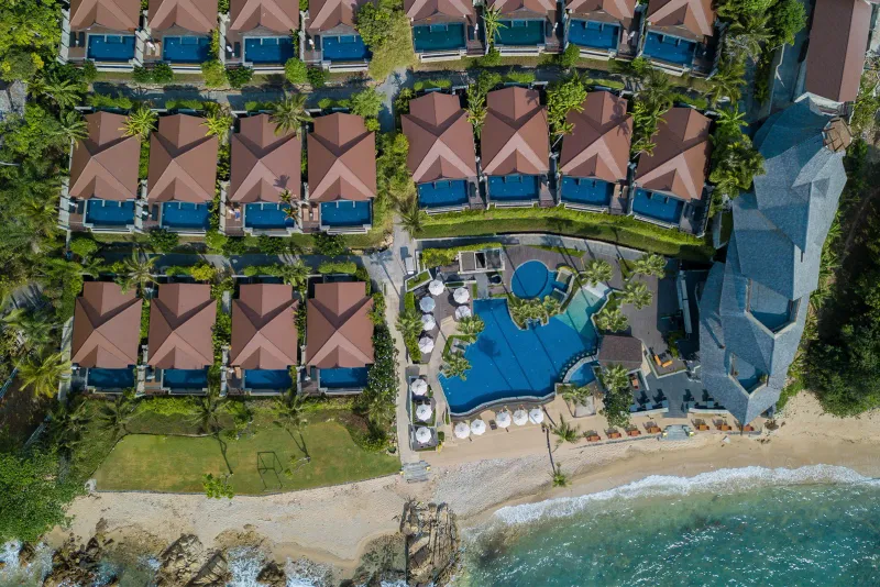 Vue aérienne des villas avec piscine du Nora Buri Resort au-dessus d'un rivage caillouteux et de la petite piscine de plage