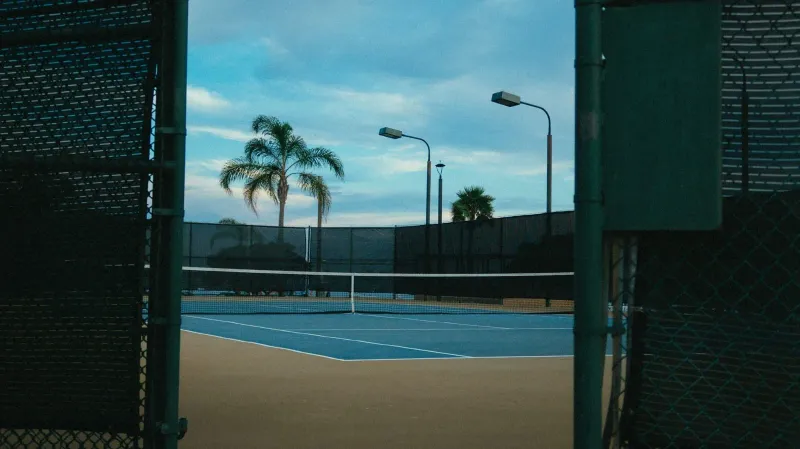 Empty daylight tennis court lined by palm trees, the daytime-only setup common at Koh Samui resorts
