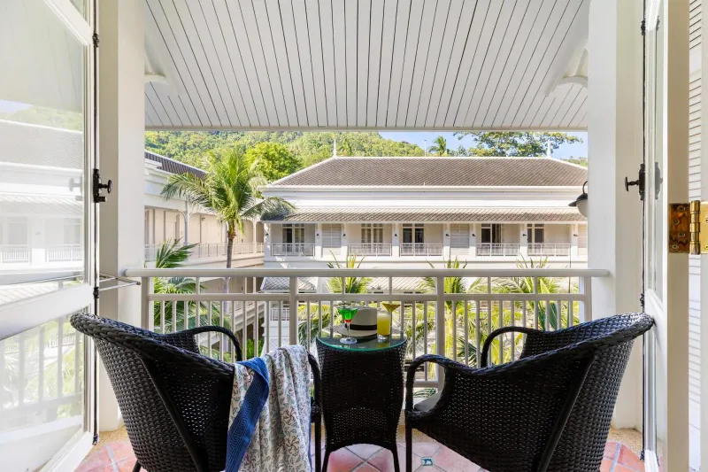 Edificio bianco in stile coloniale con balcone, sedie di rattan e palme all'Outrigger Koh Samui Beach Resort a Lamai