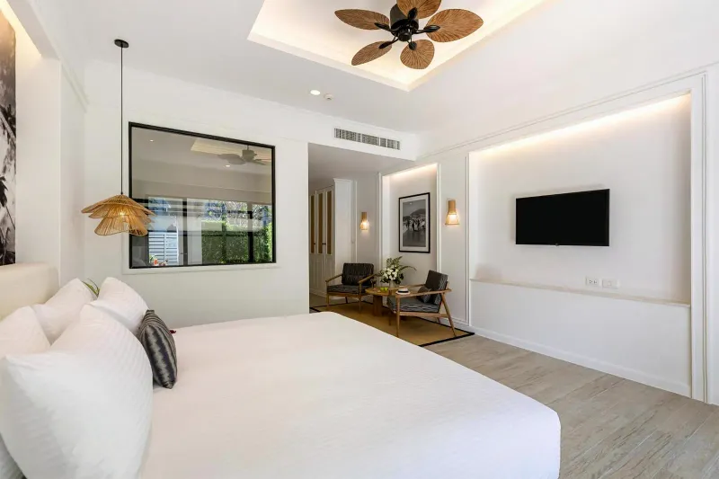 Camera luminosa e bianca con un grande letto, televisore a parete e zona salotto all'Outrigger Koh Samui