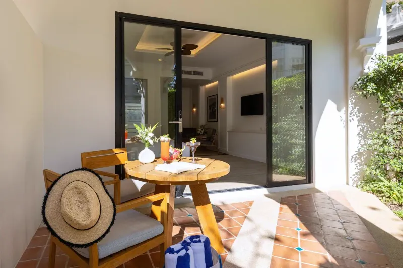 Terrazza al piano terra con sedie di canna, un tavolo rotondo e porte scorrevoli di vetro all'Outrigger Koh Samui