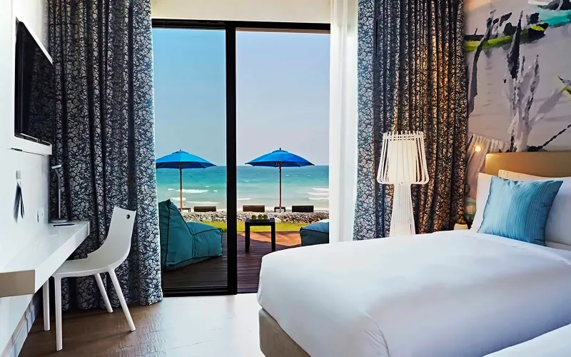 Camera dell'OZO Chaweng Samui con vista mare attraverso le porte di vetro aperte, un daybed e un ombrellone blu in terrazza