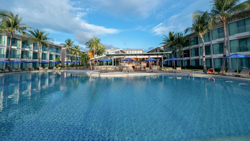 Ampia piscina dell'OZO Chaweng Samui con palme, ombrelloni blu e i blocchi di camere sullo sfondo