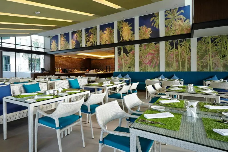 Sala da pranzo dell'OZO Chaweng Samui con sedie bianche, runner verdi sui tavoli e pannelli di vetro con stampa di palme