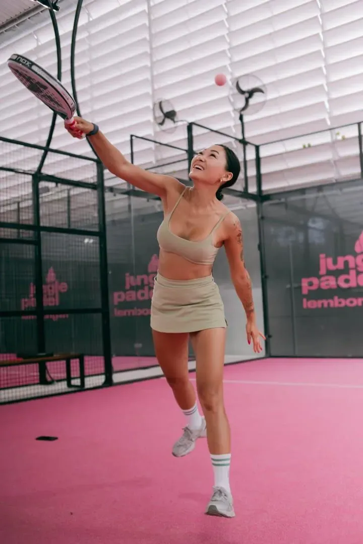 Player reaching for a shot on a pink-toned indoor padel court