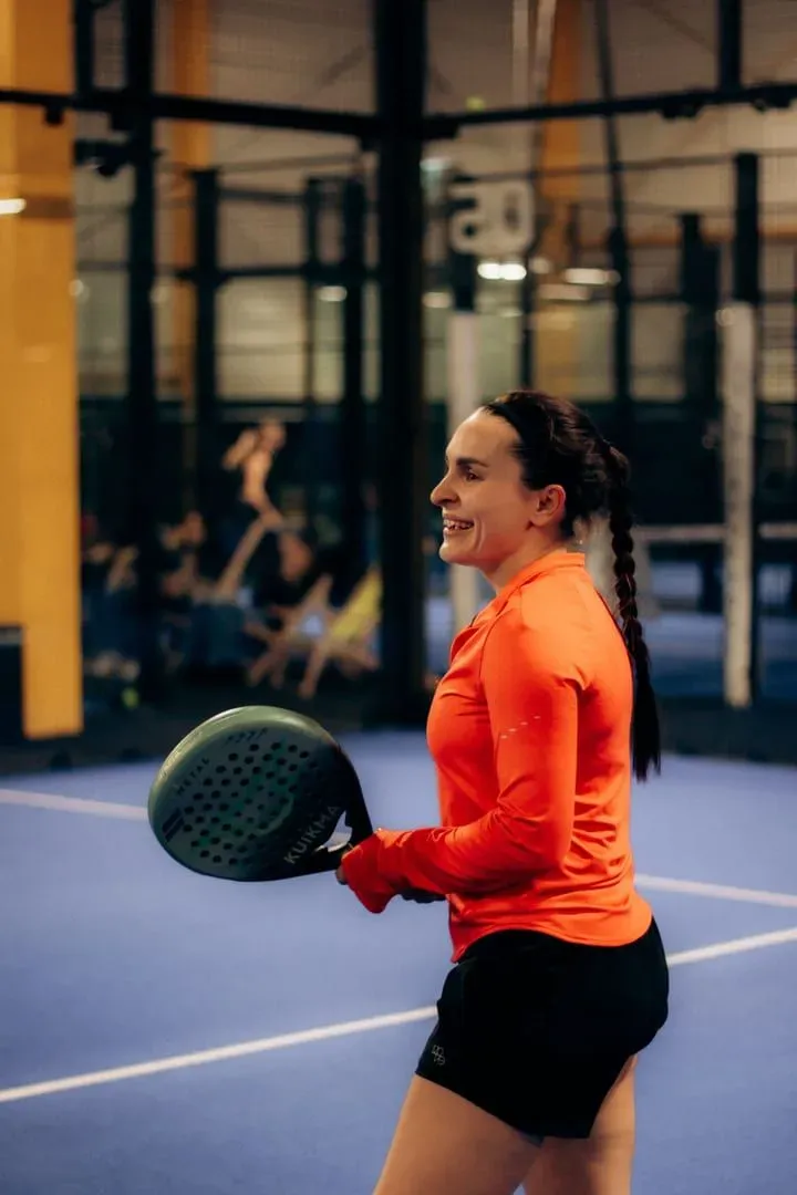 Player holding a padel paddle on a blue-surfaced indoor court between rallies
