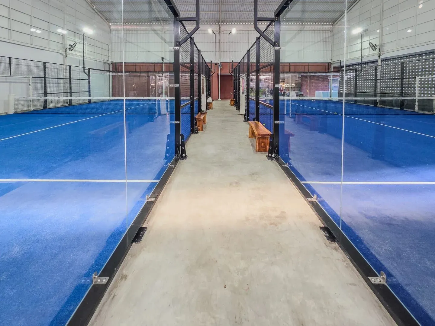 Modern indoor padel court with bright blue flooring and glass side walls, the covered-court style Samui's clubs use