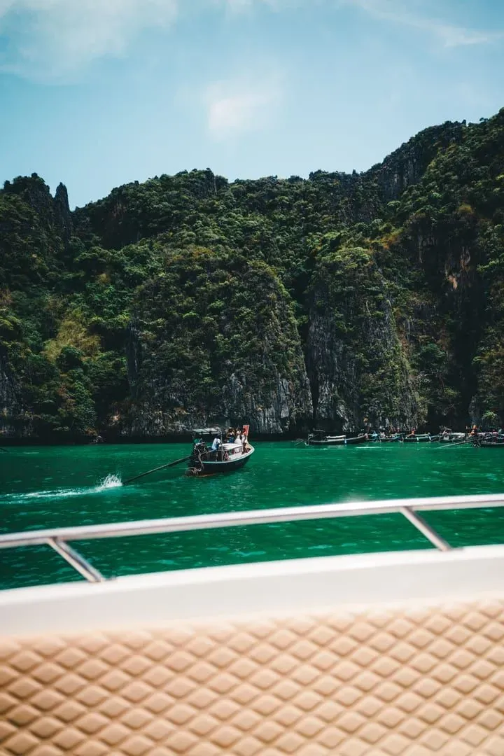 Boat crossing emerald green waters near limestone cliffs on the way from Phuket