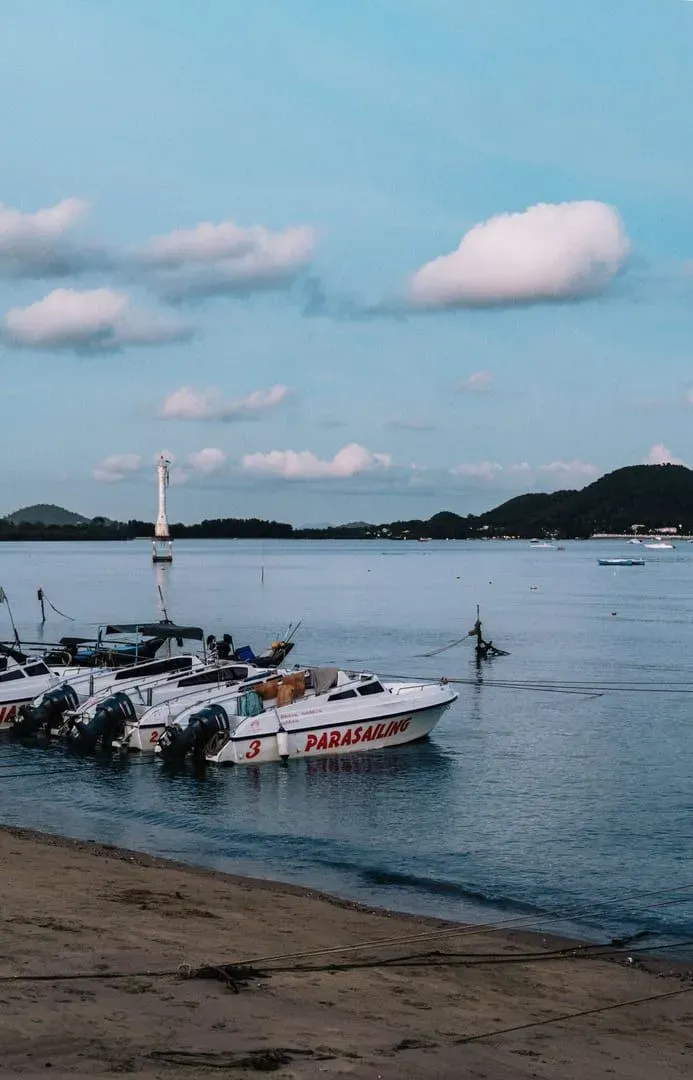 Parasailing boats docked on a Phuket beach at dusk before a bus and ferry departure