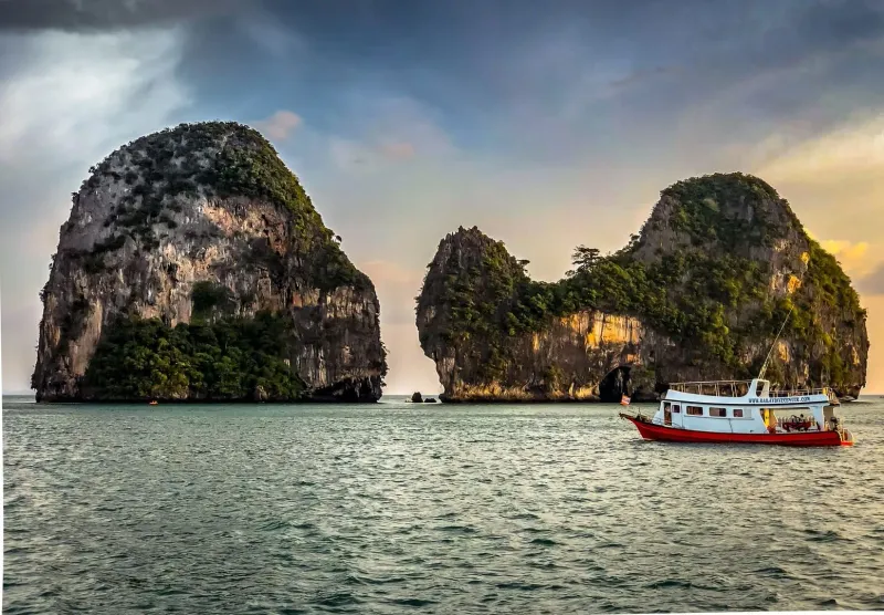 Vibrant boat sailing near limestone islands off Krabi during golden hour
