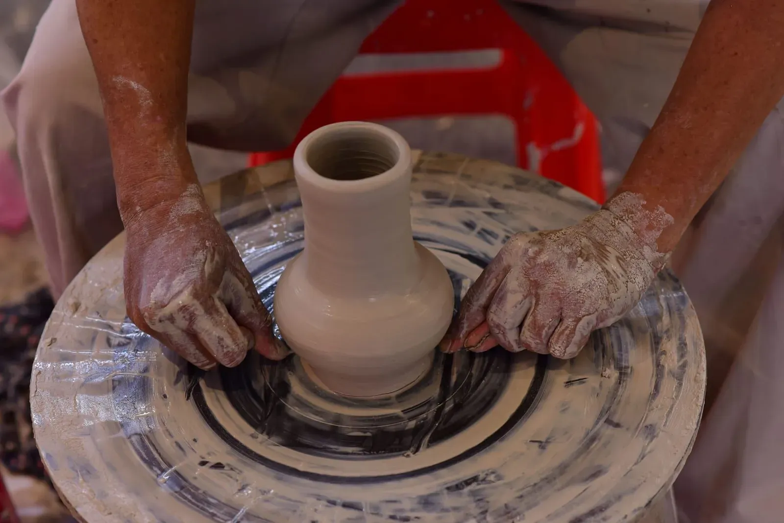 Hands shaping wet clay on a spinning pottery wheel