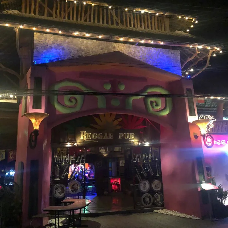 Reggae Pub's lit-up entrance archway at night, with its name spelled out above the doorway