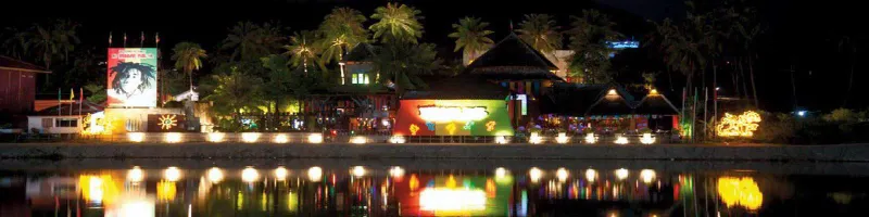 Reggae Pub's lakeside building lit up at night, viewed across Chaweng Lake with reflections on the water