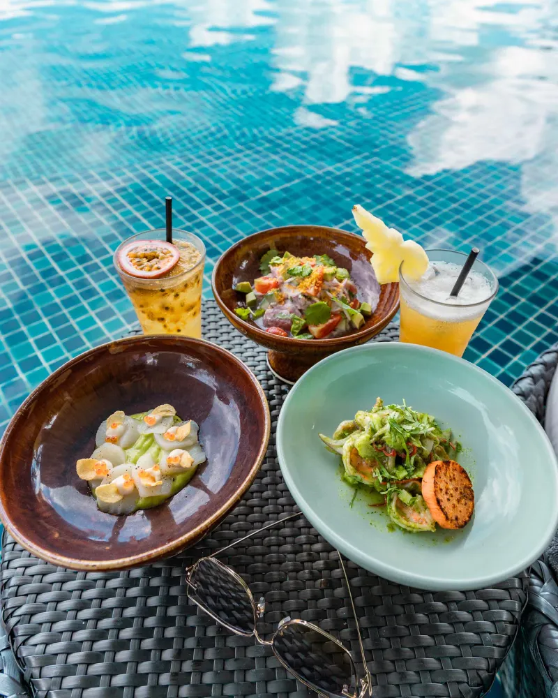 Ceviche, tartare de Saint-Jacques et deux cocktails de fruits sur une table au bord de la piscine