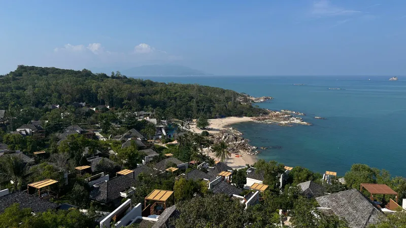 Vue en hauteur des toits du resort, de la petite plage de sable et du rivage rocheux de la baie privée