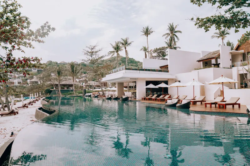 Piscine incurvée du resort avec bar, transats et palmiers au bord de la plage de The Ritz-Carlton, Koh Samui