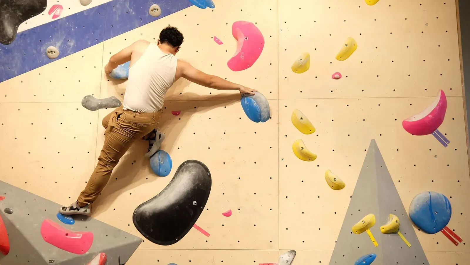 Climber stretching between two holds on a bouldering wall, the indoor training style Samui's own sports park now confirms