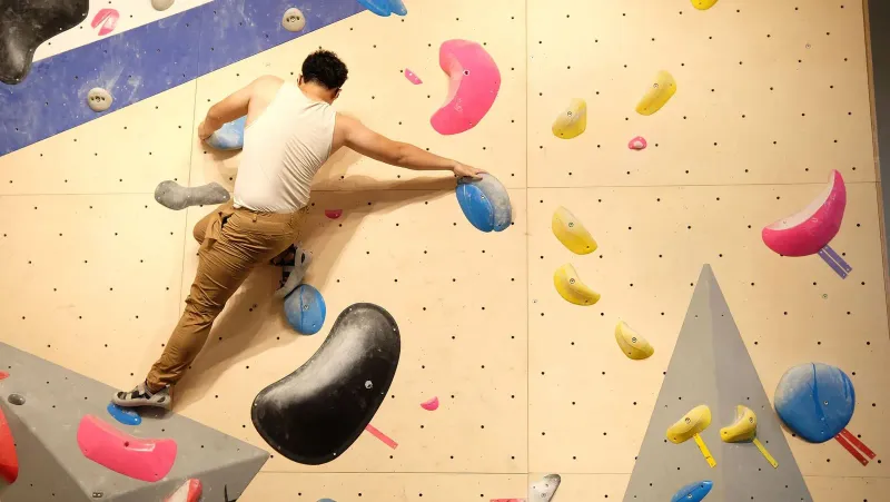 Arrampicatore che si allunga fra due prese su un muro boulder, lo stile di allenamento indoor che il parco sportivo di Samui ora conferma