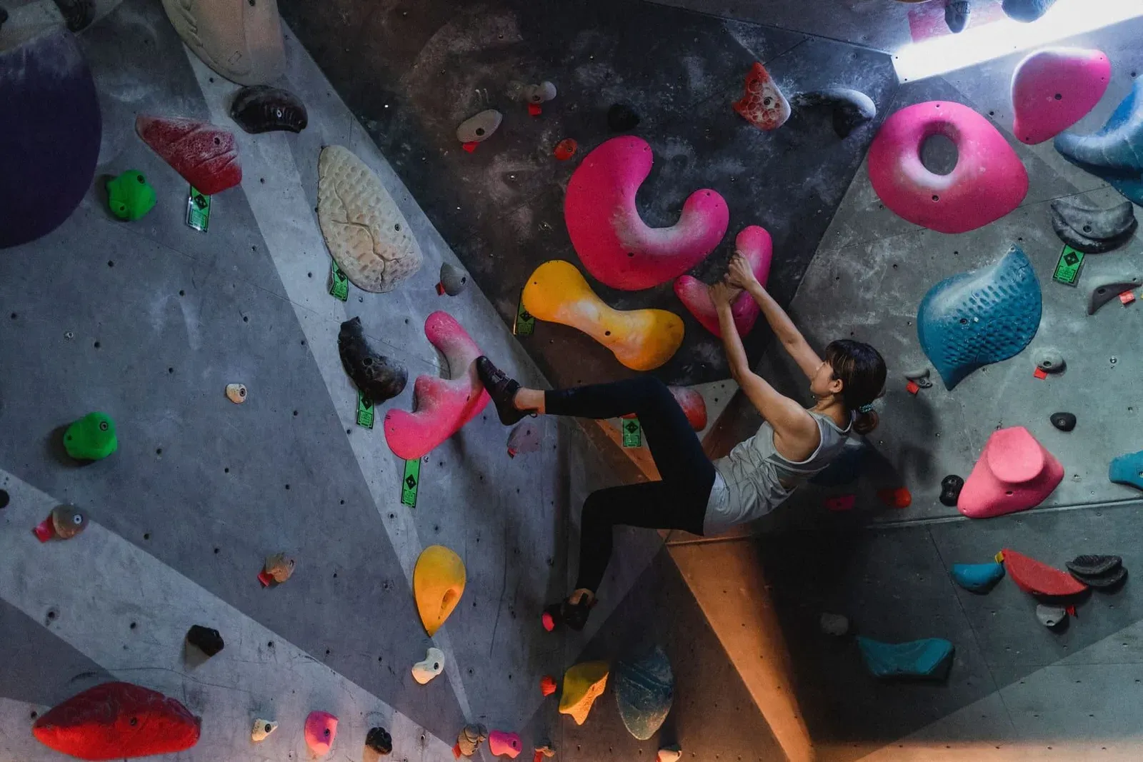 Climber reaching for a pink hold on a colourful indoor bouldering wall, the training style now confirmed at one Bophut sports park