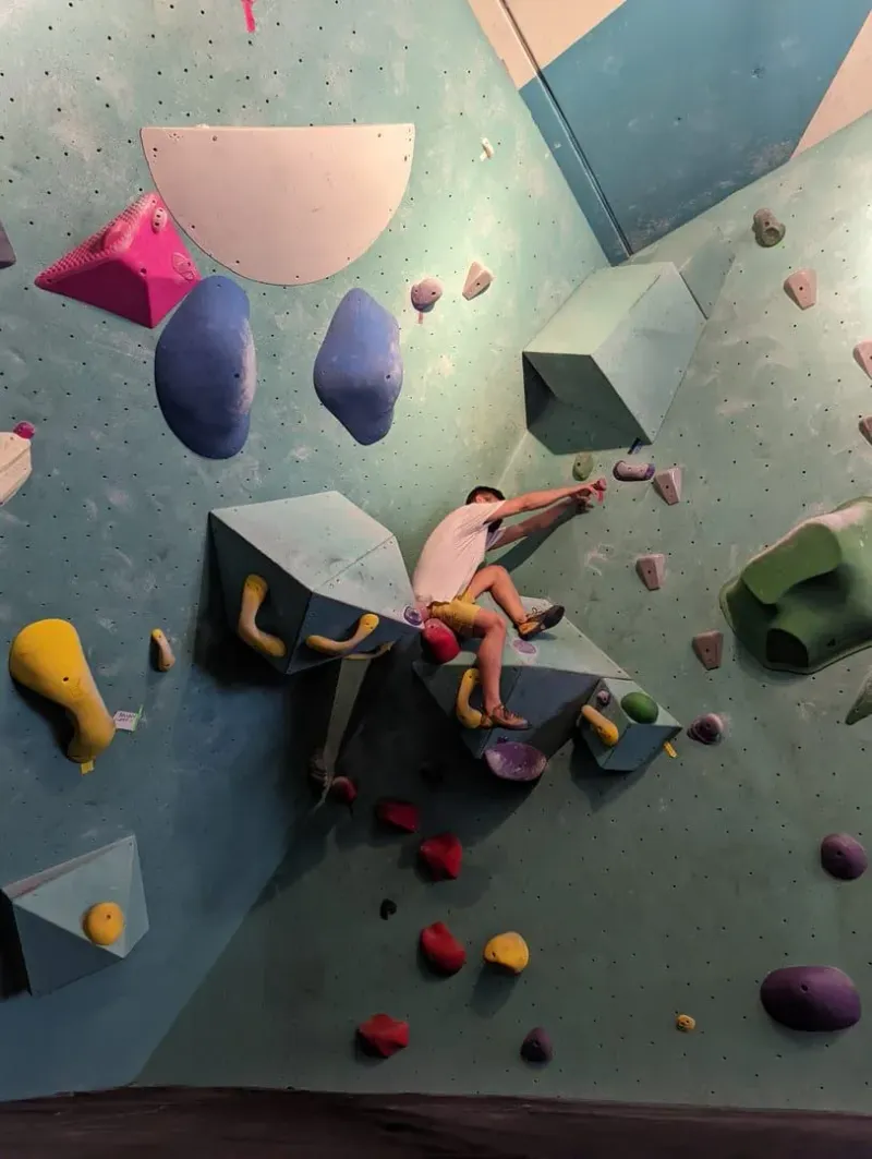 Climber reaching across an angled bouldering wall studded with colourful volumes and holds