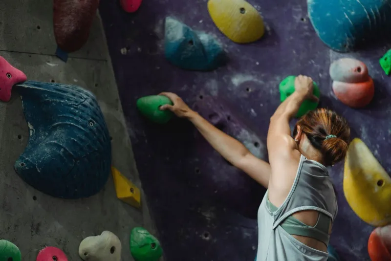 Close-up of a climber's chalked hand gripping a green hold mid-route on an indoor wall