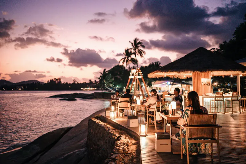 Tramonto sulla baia con tavoli illuminati sulla spiaggia tra le rocce al Rocky's Boutique Resort a Lamai