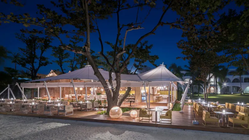 Le restaurant de plage The Tent au SALA Samui Chaweng illuminé le soir, auvents blancs sous les arbres