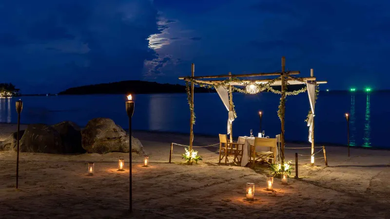Table de dîner privée sur la plage sous un auvent éclairé par des torches, le soir, au SALA Samui Chaweng