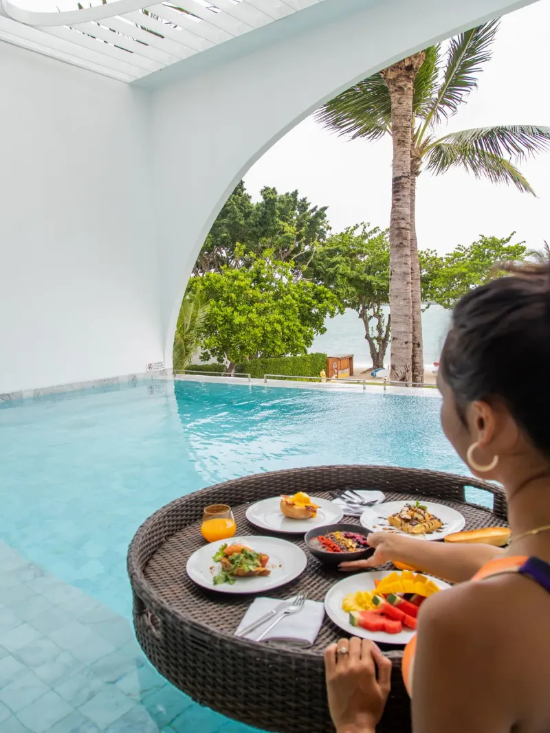Plateau de petit-déjeuner flottant dans une piscine privée du SALA Samui Chaweng, avec vue sur la plage à travers une paroi à arche