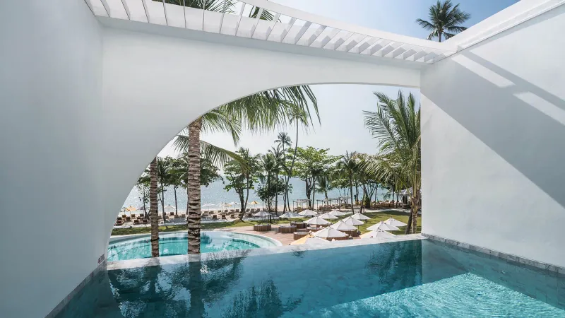 Suite avec piscine et balcon face à la mer au SALA Samui Chaweng, petite piscine à l'arche blanche encadrant palmiers et plage