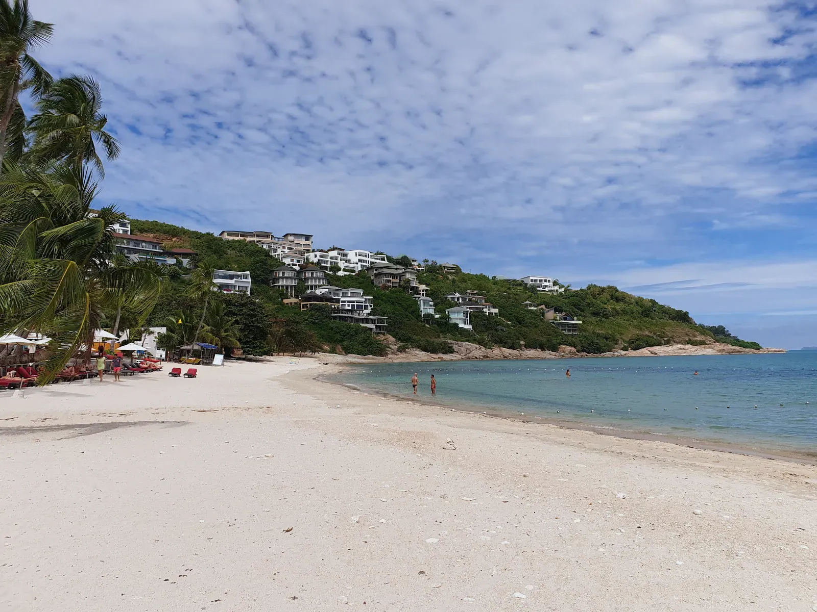 Geschwungener weißer Sand an Thongson Bay, im Hintergrund Villenresorts am Hang