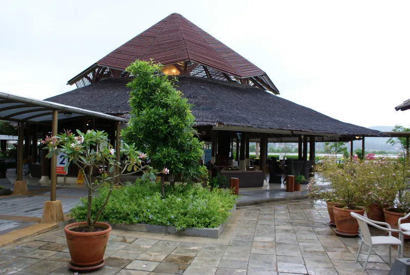 Toit de pavillon en chaume et frangipaniers dans la zone de départs intérieurs en plein air de l'aéroport de Samui
