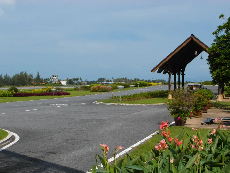 Aire en plein air de l'aéroport international de Samui avec un abri à toit de bois et la tour de contrôle au fond