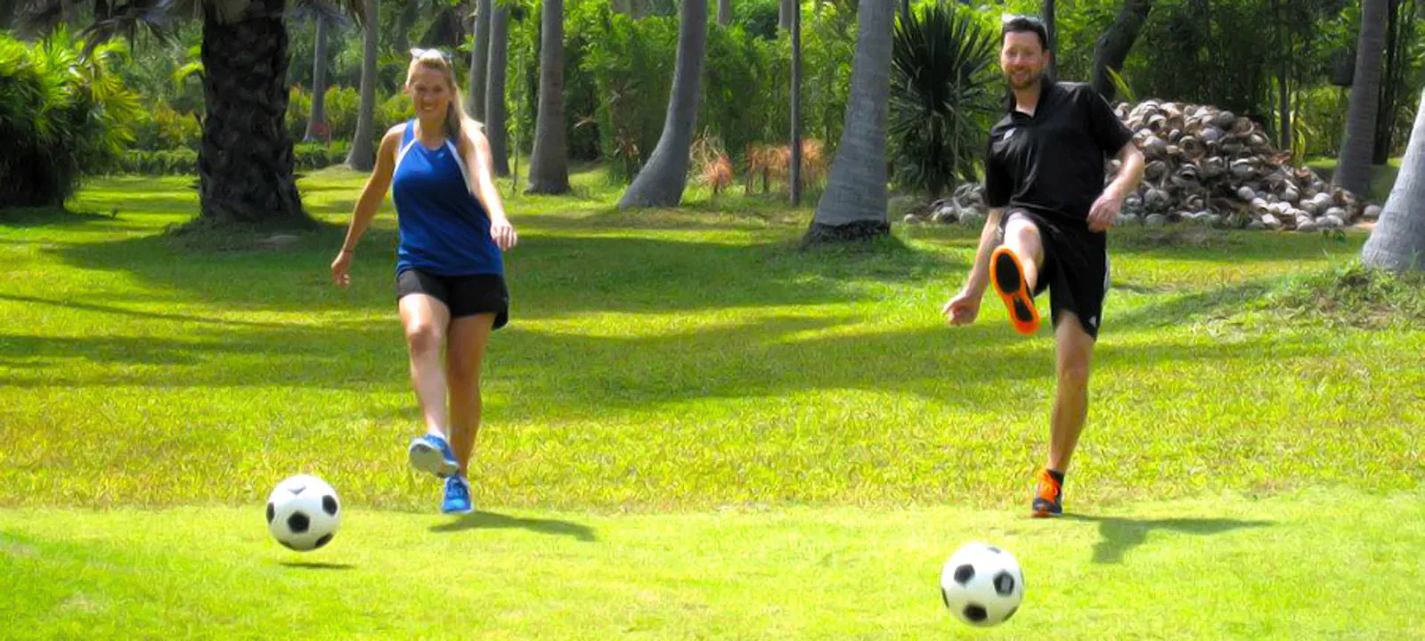 Two players kicking footballs across the grass fairway at Samui Football Golf's botanical garden course