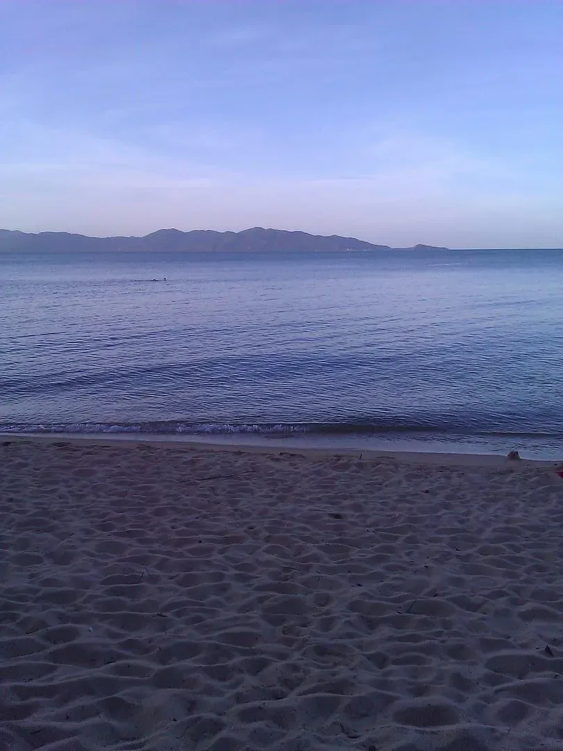 View across calm water from Maenam Beach toward a mountainous island silhouette in the evening light