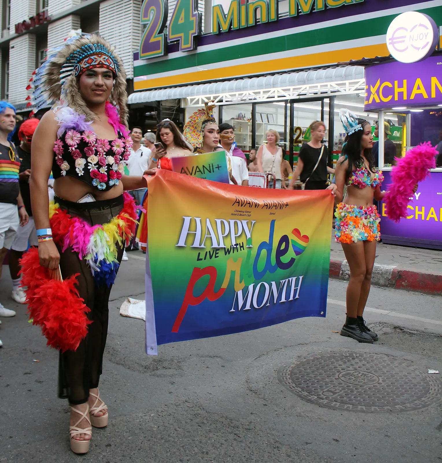 Performers in feathers and flowers holding a Pride Month banner during the Samui Pride parade