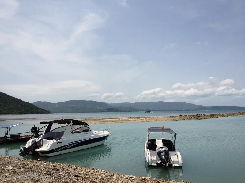 岩の多いサムイ島の岸辺沖、ターコイズブルーの浅瀬に停泊する2隻の小型スピードボートと、その奥の丘