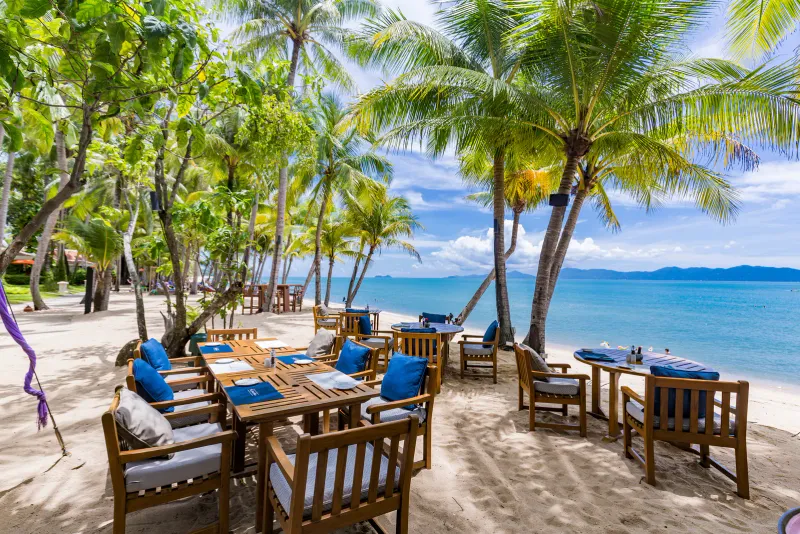 Tables en bois sur le sable sous les cocotiers au bord de la mer à Santiburi Koh Samui