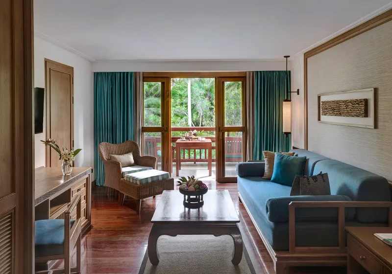 Salon d'une suite avec canapé bleu pétrole, parquet sombre et portes-fenêtres de balcon sur le jardin à Santiburi Koh Samui