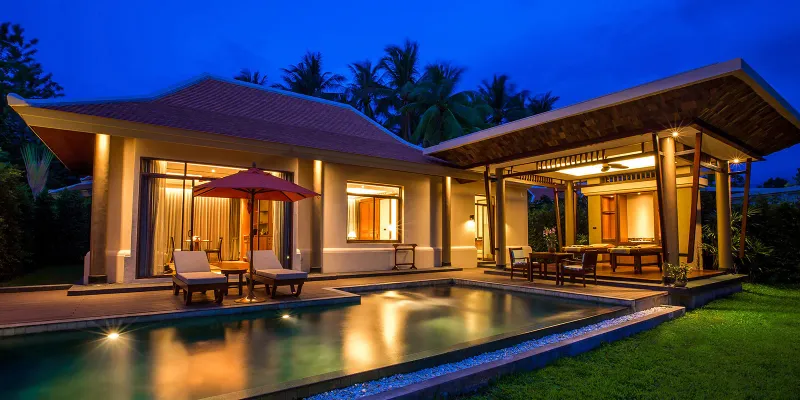 Villa avec piscine éclairée au crépuscule, terrasse allumée, parasol rouge et transats à Santiburi Koh Samui