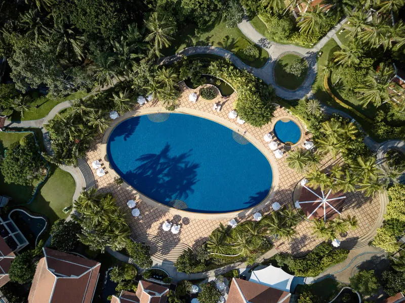 Vue aérienne de la grande piscine ovale entourée de jardins et de bâtiments aux toits rouges à Santiburi Koh Samui